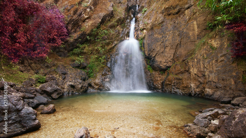 unseen waterfall with clear green water with red leaves and rock for relax and refreshing cool with tree and gravel in jungle or forest at Jokkradin waterfall for nature landscape on summer autumn