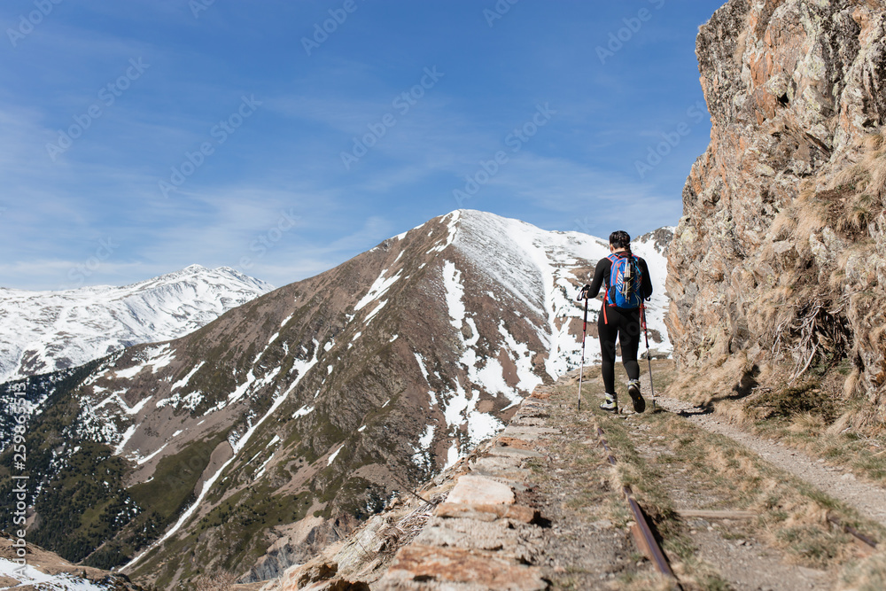 Rear view of hiker woman walking by a cliff in a sunny day mountains background Rear view of hiker woman walking by a cliff in a sunny day mountains background