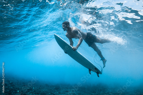 Surfer performs dive (the duck dive) with his surfboard under the wave