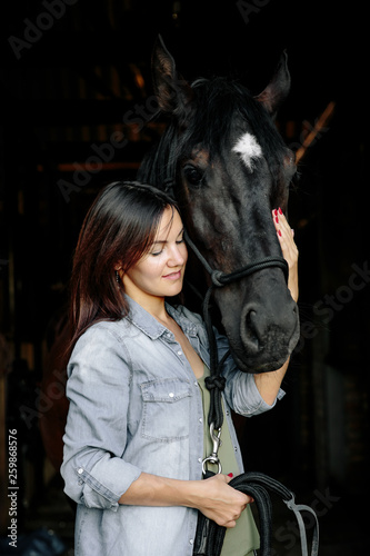 Portrait of elegant young woman holding her black horse outdoors.