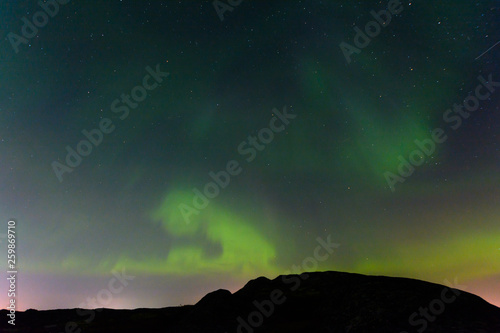 Green northern lights over the hills, aurora. © Moroshka