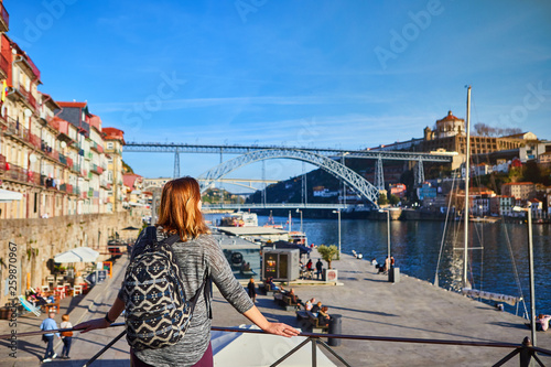 Young woman traveler standing back enjoying beautiful cityscape view on Douro river, bridge and boats during the morning light in Porto, Portugal
