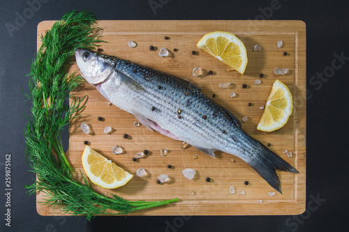 Grey mullet fish on the wooden board wıth lemon, onion and spices.