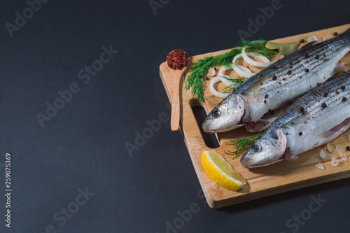 Grey mullet fish on the wooden board wıth lemon, onion and spices.