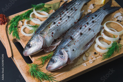 Grey mullet fish on the wooden board wıth lemon, onion and spices.