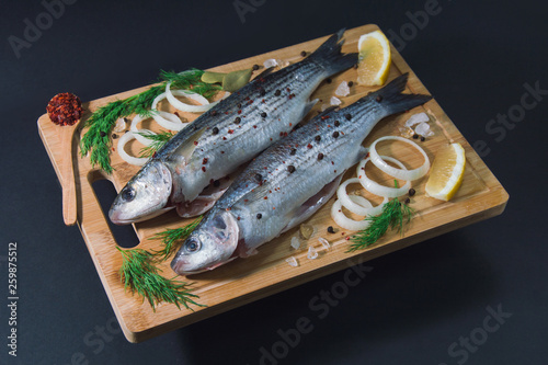 Grey mullet fish on the wooden board wıth lemon, onion and spices.