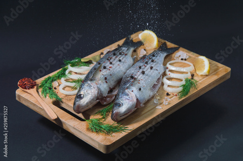 Pouring the salt onto the grey mullet fish on the wooden board wıth lemon, onion and spices.