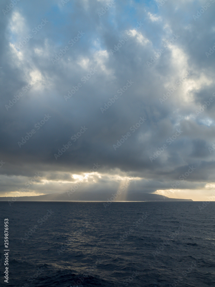 Sun rays burst out from behind clouds over the ocean