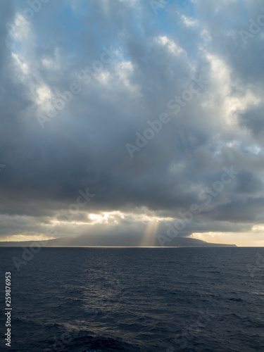 Sun rays burst out from behind clouds over the ocean