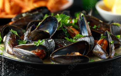 Mussels with white wine, garlic, lemon and herbs in a plate, French fries. rustick background. Seafood.