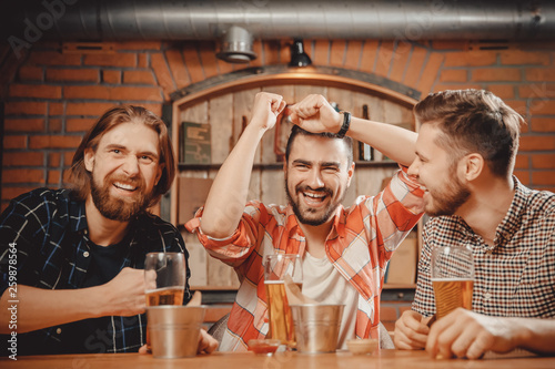 Cheerful friends men fans watch sports match on TV and drink draft beer in bar pub photo