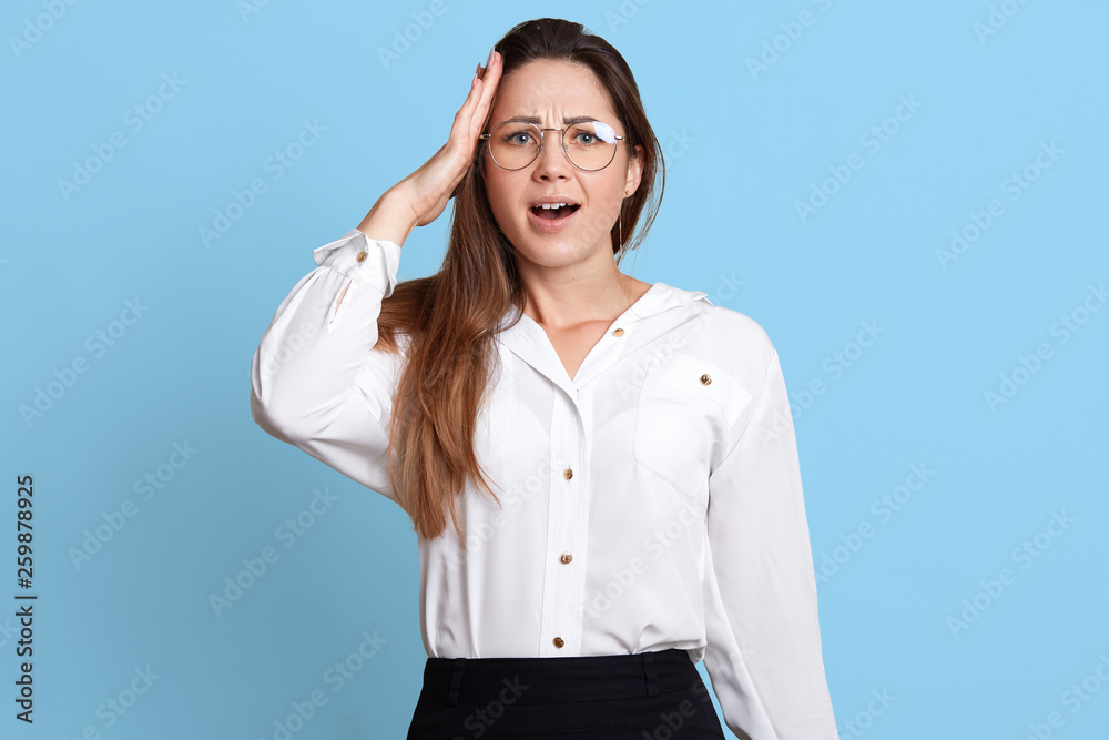 Worrying busy accountant holds her hand on head, remembers about important work assignment, opens her mouth with surprise. Slender attractive woman is short of time to complete all working tasks. Worrying busy accountant holds her hand on head, remembers about important work assignment, opens her mouth with surprise. Slender attractive woman is short of time to complete all working tasks.