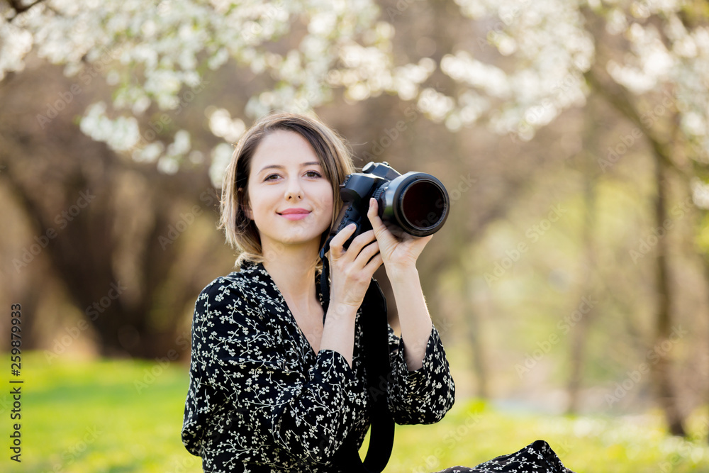 Young girl with camera sitting near a flowering tree i Young girl with camera sitting near a flowering tree i