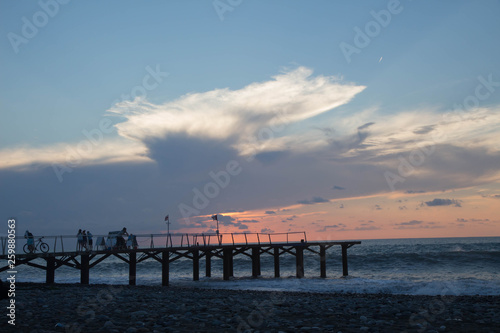 sun setting over Batumi beach pier, as powerful waves roll in, and a very colorful sky is reflected on the beach