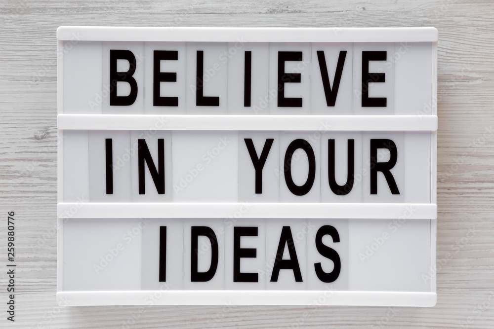 'Believe in your ideas' words on modern board over white wooden surface, top view. Flat lay, from above, overhead.