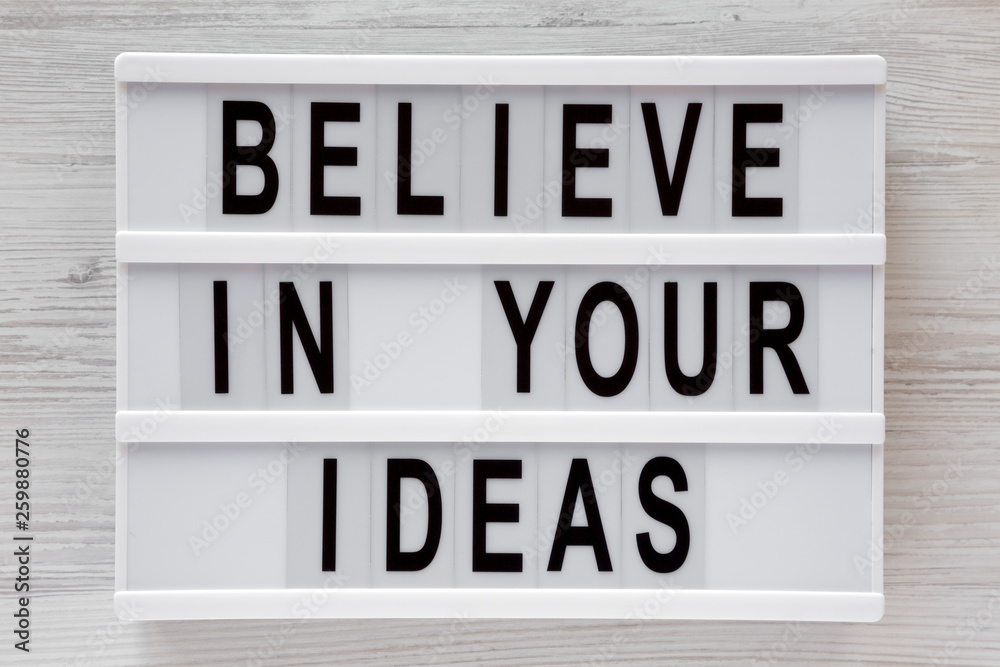 'Believe in your ideas' words on modern board over white wooden surface, top view. Flat lay, from above, overhead. 'Believe in your ideas' words on modern board over white wooden surface, top view. Flat lay, from above, overhead.