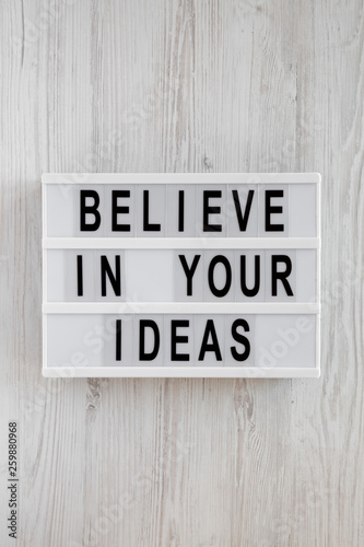 'Believe in your ideas' words on modern board over white wooden surface. Flat lay, from above, overhead.
