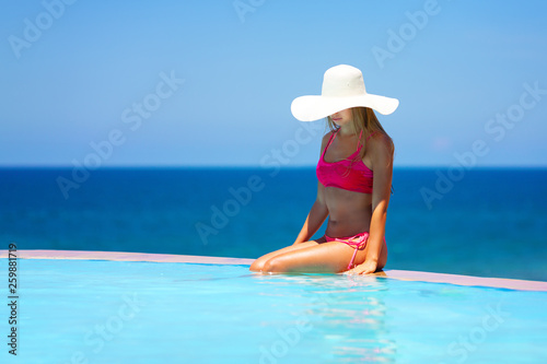 Summer vacation travel beach photo - young pretty blonde girl with sexy body relaxing on tropical exotic infinity pool in bikini in white hat on Maldive