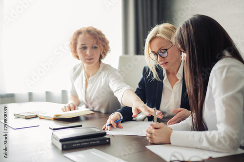 Female business team of young attractive employees discuss online project in modern office, collaborating using notepads for notes.