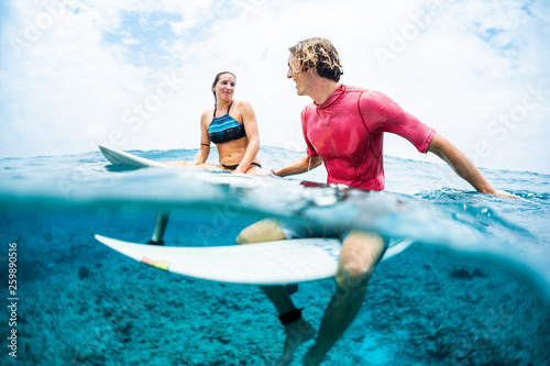 Two young surfers sit on their boards in the tropical ocean