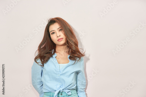 Beautiful lady in trendy blue blouse looking at camera with confident face expression while standing on light pink background