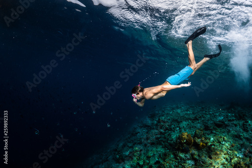 Young man snorkeling and skin diving over the coral reef edge in the tropical sea
