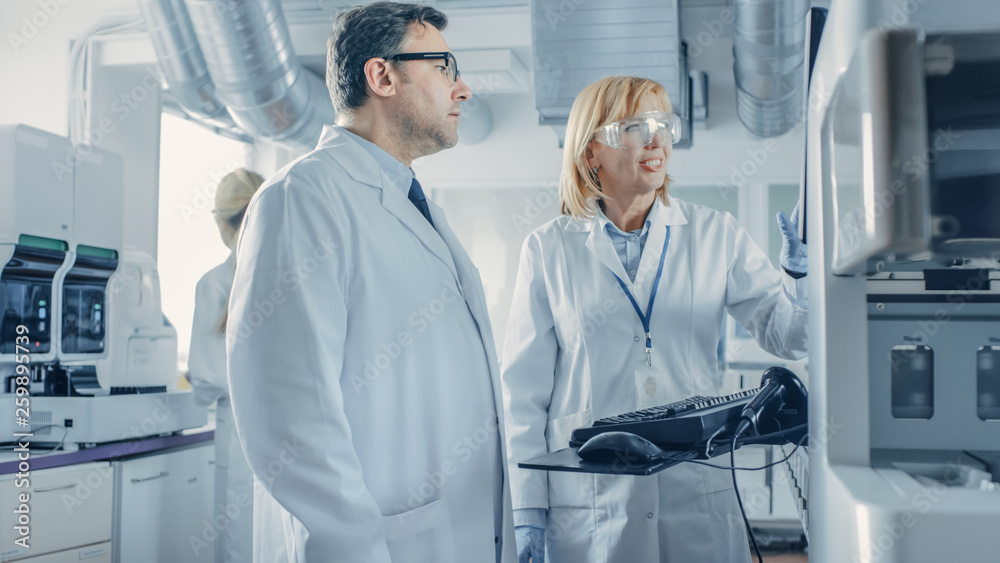 Two Research Scientists Talking about Programming Medical Equipment for Tests. Team of Professionals Doing Pharmaceutical Research in Modern Laboratory