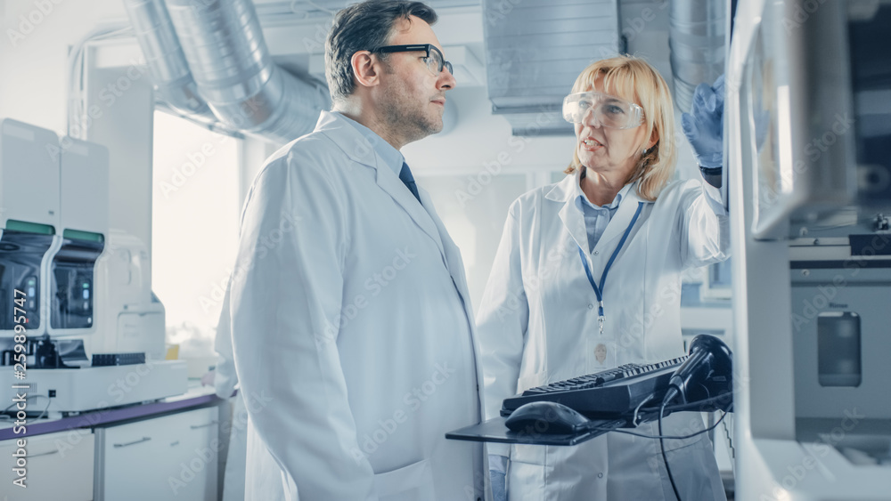 Obraz premium Two Research Scientists Talking about Programming Medical Equipment for Tests. Team of Professionals Doing Pharmaceutical Research in Modern Laboratory