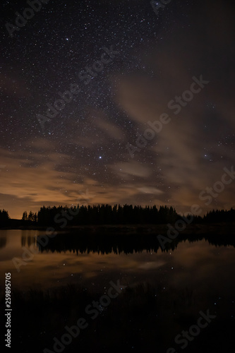 Night sky with starts in a Conemara lake with Pine Forest around