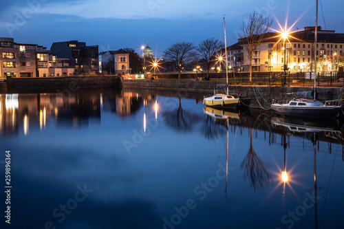 Building, houses, boats around Corrib river with Cathedral in background in Galway