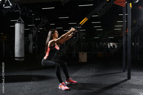 Beautiful fitness woman training with trx fitness straps. Suspension exercising in gym