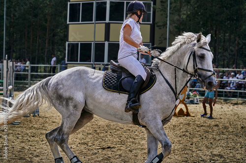 Young woman jockey in white dress and black boots takes part in equestrian competitions. Close-up.