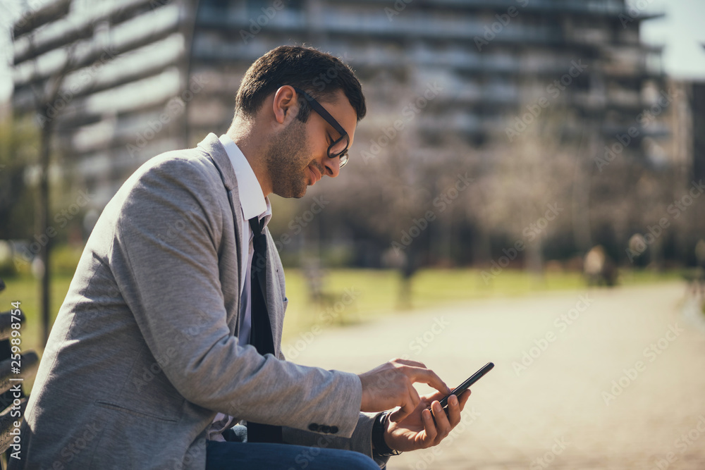 Fototapeta premium Young businessman is using smartphone in park.