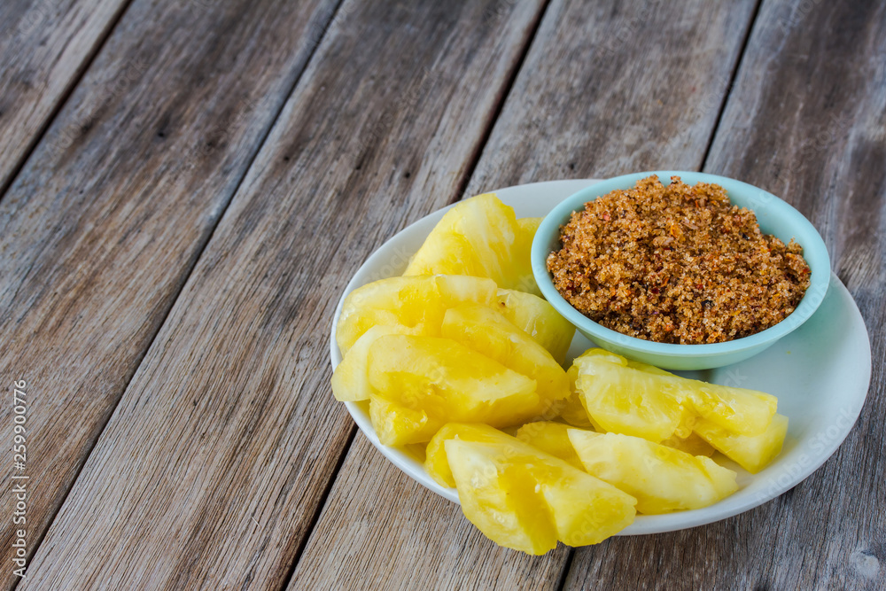 pineapple in plate.sugar and chili in a cup on a wooden table. pineapple in plate.sugar and chili in a cup on a wooden table.