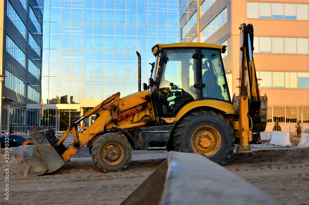 Yellow tractor, wheel loader with a bucket on road works in the city on the background of a business center