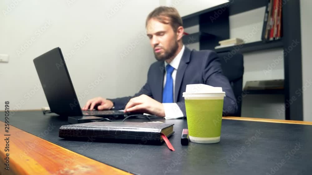 A man working on a laptop in his office finds lip gloss left by someone on his desk. A man working on a laptop in his office finds lip gloss left by someone on his desk.