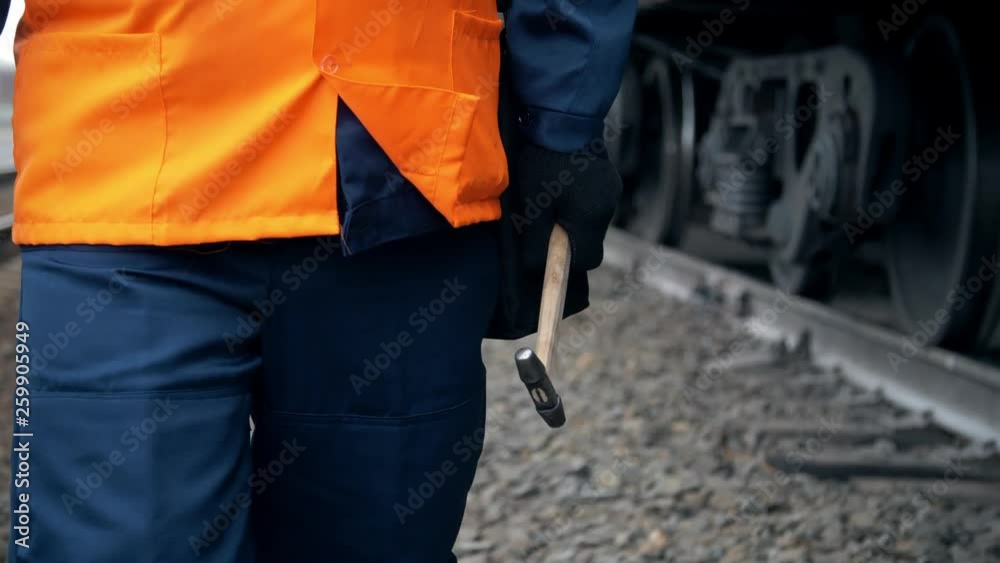 Worker in orange workwear walks near a railroad train car.