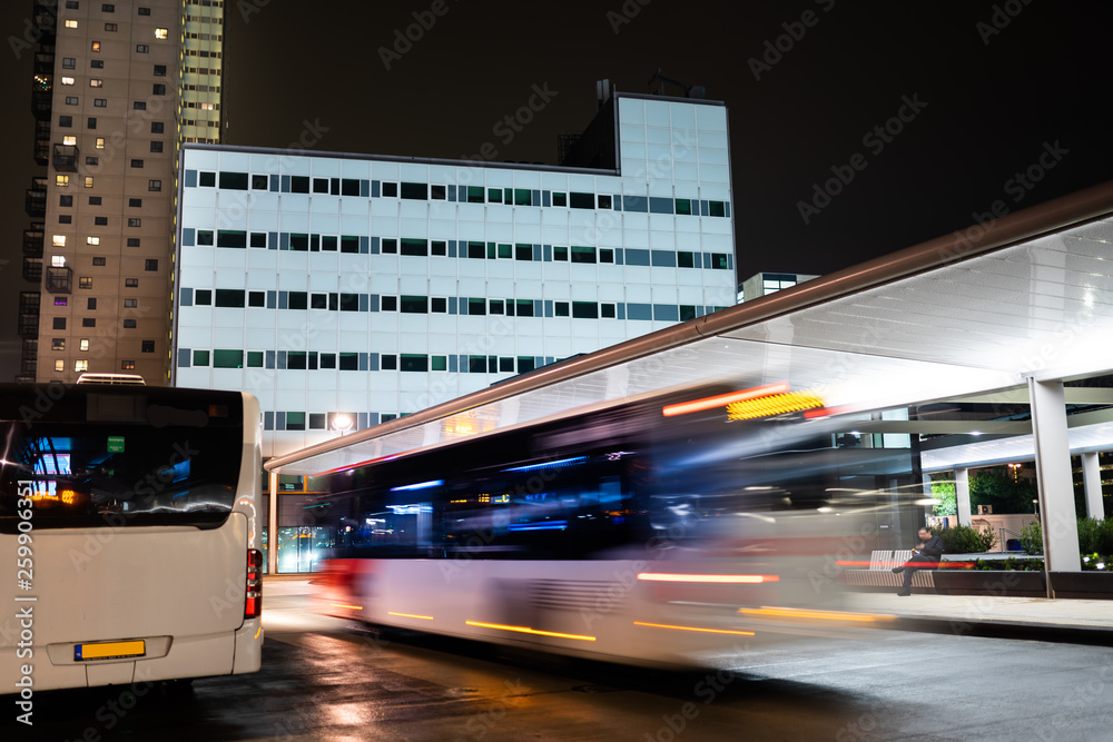 Tilburg, Noord Brabant, Netherlands - april 2 2019: A bus driving next to the bus station and train station. This is the new public transport hub in Tilburg next to a scyscraper tower. Seen at night.
