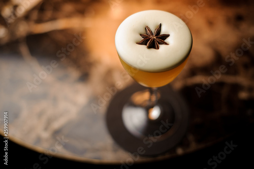 Cocktail with the white foam in the glass decorated with the one anise star standing on the marble table