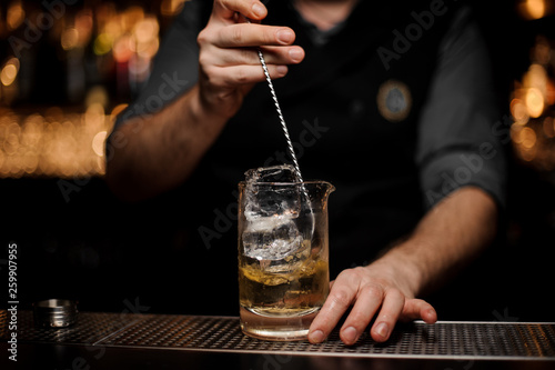 Barman stirring a delicious cocktail with a steel spoon in the measuring glass cup