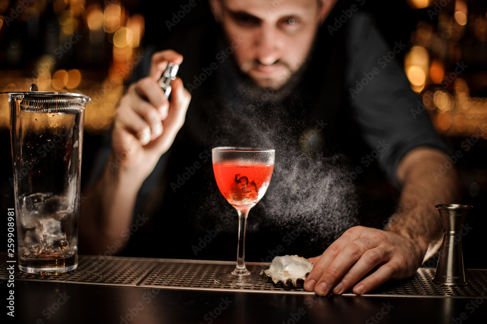Bartender spraying on the delicious transparent red cocktail in the glass
