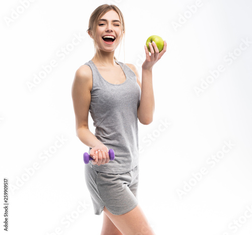 Sporty fit woman holding dumbbells weights in one and apple fruit in another hand. Fitness and healthy dieting concept.