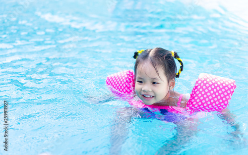 little asian girl wearing inflatable sleeves swimming in the pool