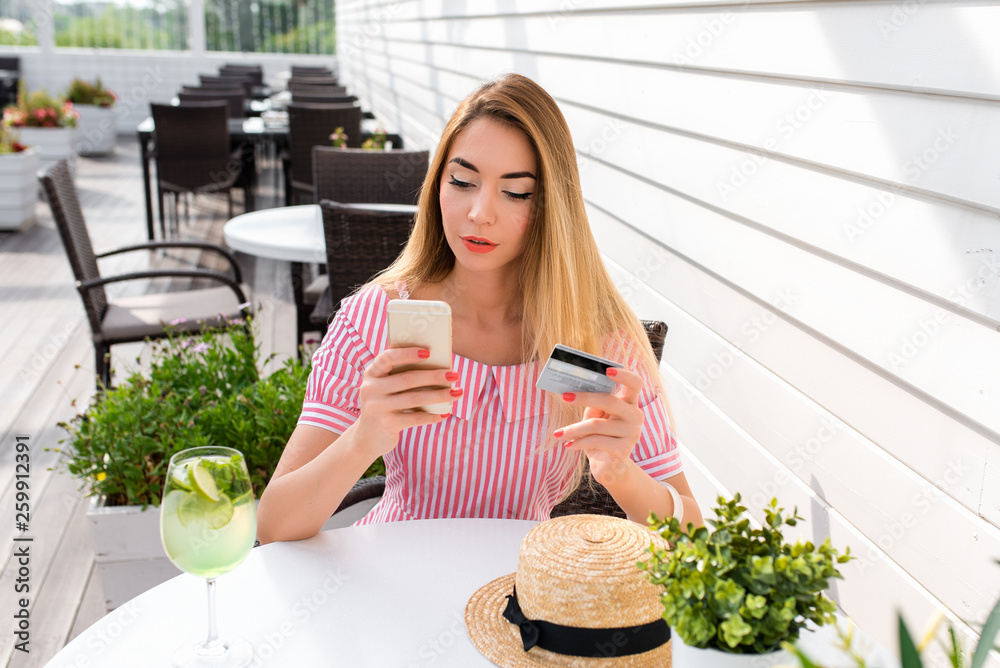 A woman in a cafe in summer in city, pays lunch breakfast dinner, plastic credit card, online internet application. Enters a password, debits money from account. Activates discount and promo code.