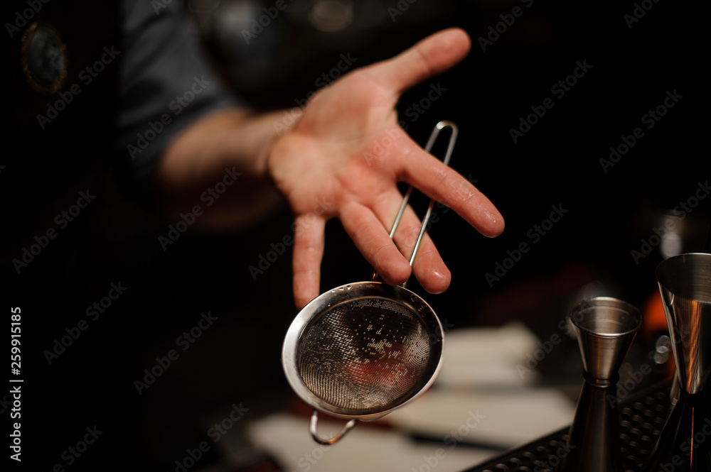 Professional bartender holding in hand a steel sieve