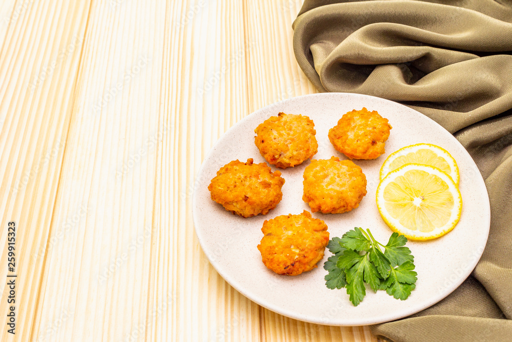 Homemade red fish cakes with lemon and parsley in ceramic plate. With fabric drapery on wooden background, copy space.