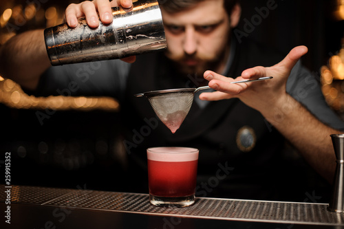 Bartender pouring a smooth pink cocktail through the sieve to the glass