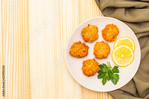 Homemade red fish cakes with lemon and parsley in ceramic plate. With fabric drapery on wooden background, copy space, top view.