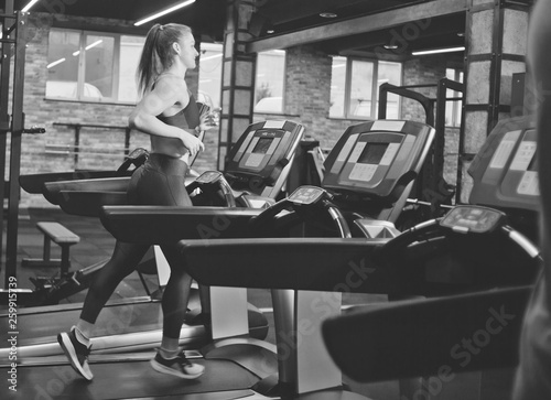 Young sports woman doing cardio training on treadmill. Running on treadmill at gym. Black and white photo