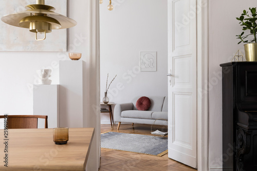Modern scandi interior of living room with design wooden table  chairs  sofa and white stands with stylish accessories. Abstract paintings on the wall. Elegant home decor. Mock up poster frame. 